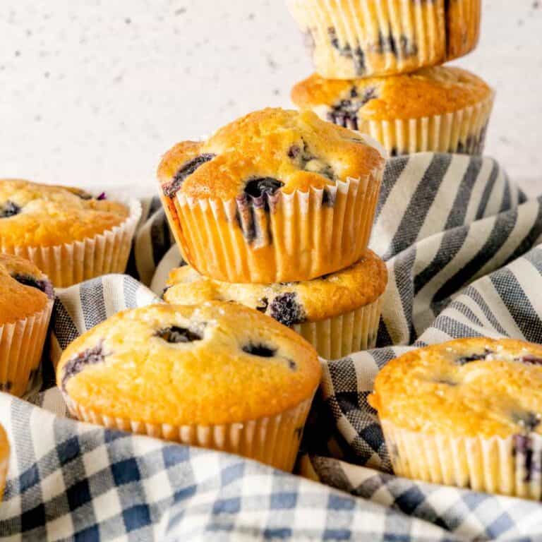 Freshly baked old fashioned blueberry muffins recipe in white muffin liners on a blue checkered napkin.