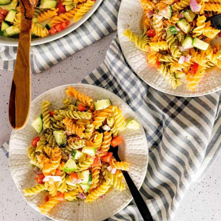 Two plates and a serving dish of oil and vinegar pasta salad.