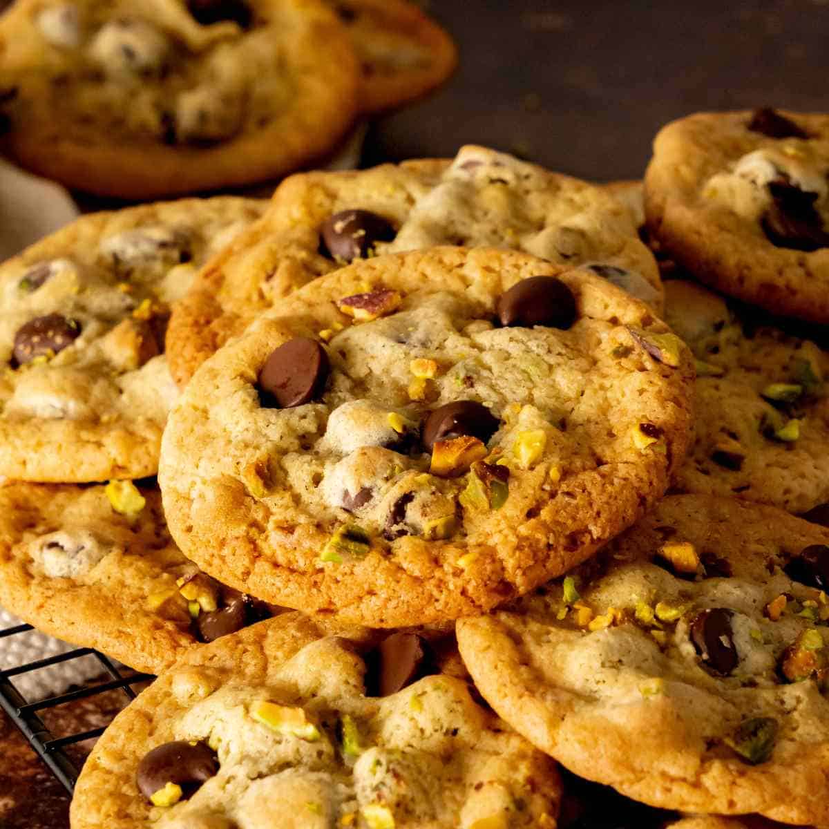 Pistachio chocolate chip cookies stacked on a square cooling rack.