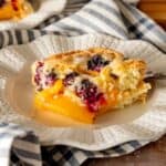A slice of blueberry peach cobbler cake on a decorative plate with a black fork.