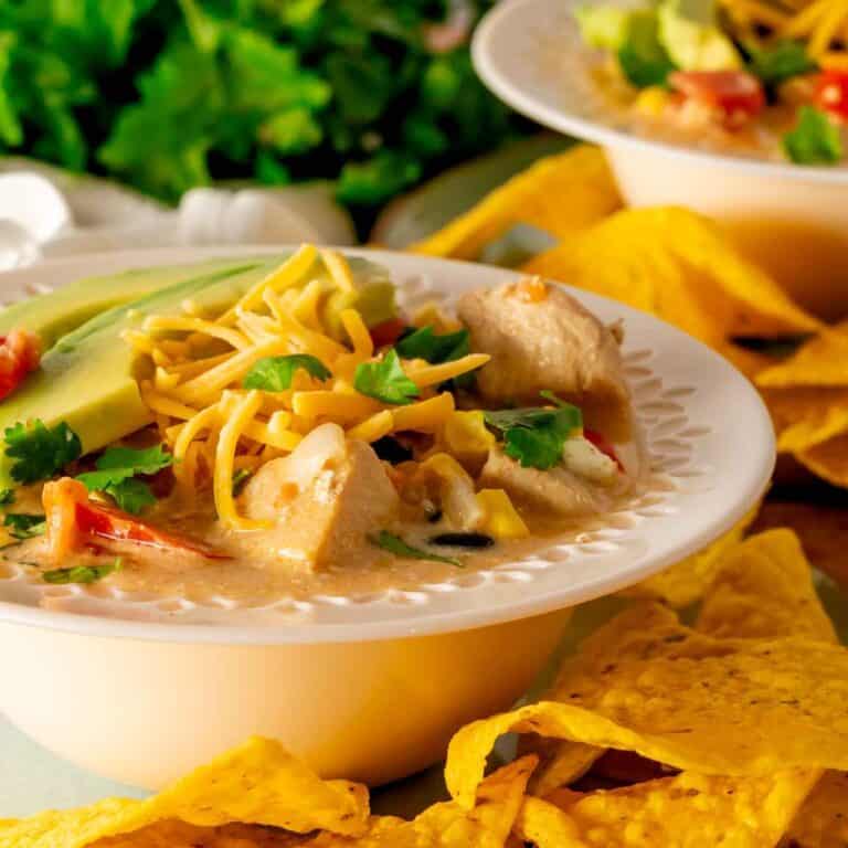 A rimmed bowl with chicken taco soup garnished with cheese, avocado slices, and tortilla chips.