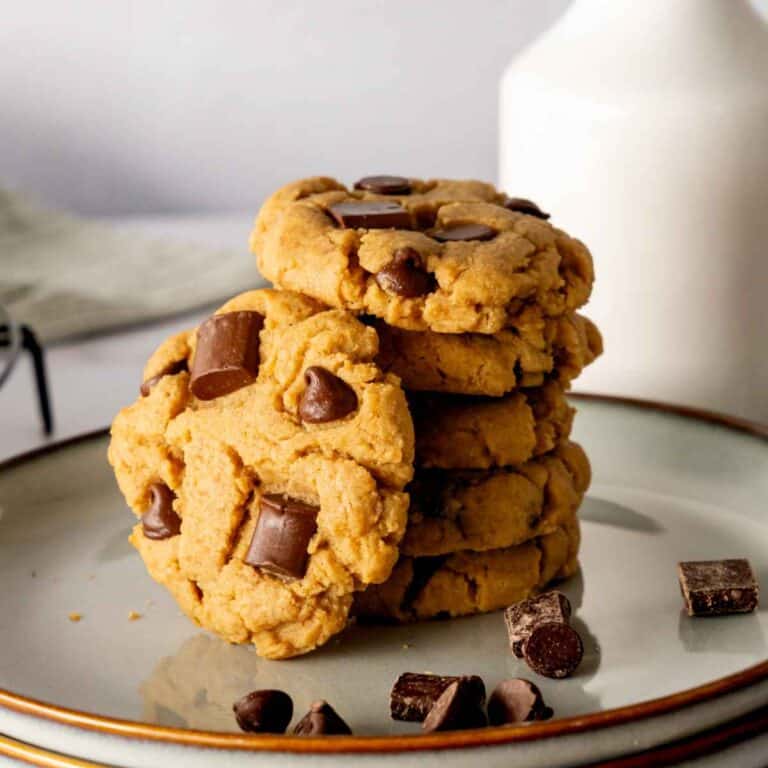 A stack of peanut butter chocolate chip cookies on a plate with a glass of milk behind it.