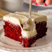 Red Velvet Brownie with cream cheese frosting on a white plate and a fork cutting through it.