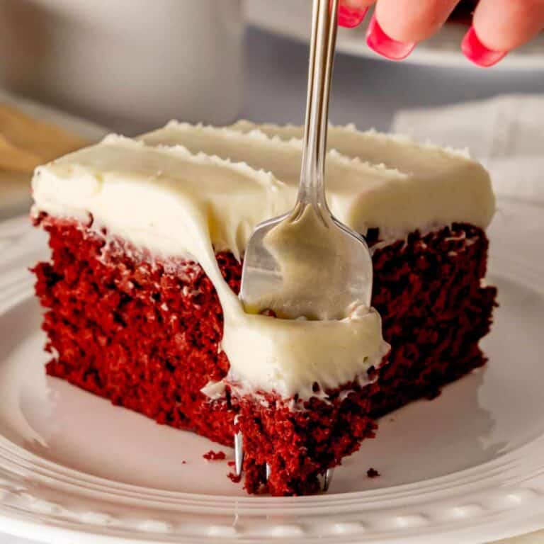 Red Velvet Brownie with cream cheese frosting on a white plate and a fork cutting through it.
