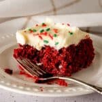 A slice of red velvet poke cake topped with cream cheese frosting.
