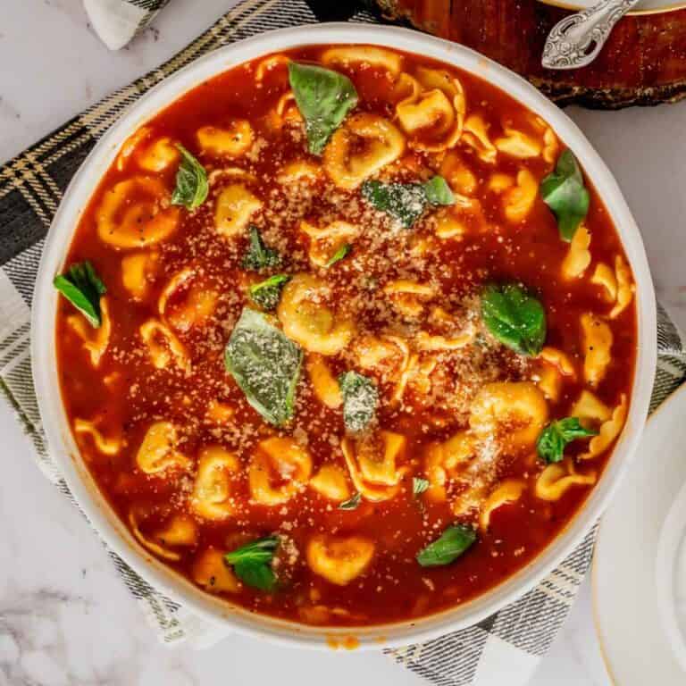 Tomato Basil Tortellini Soup in a large serving bowl with fresh basil and Parmesan cheese.