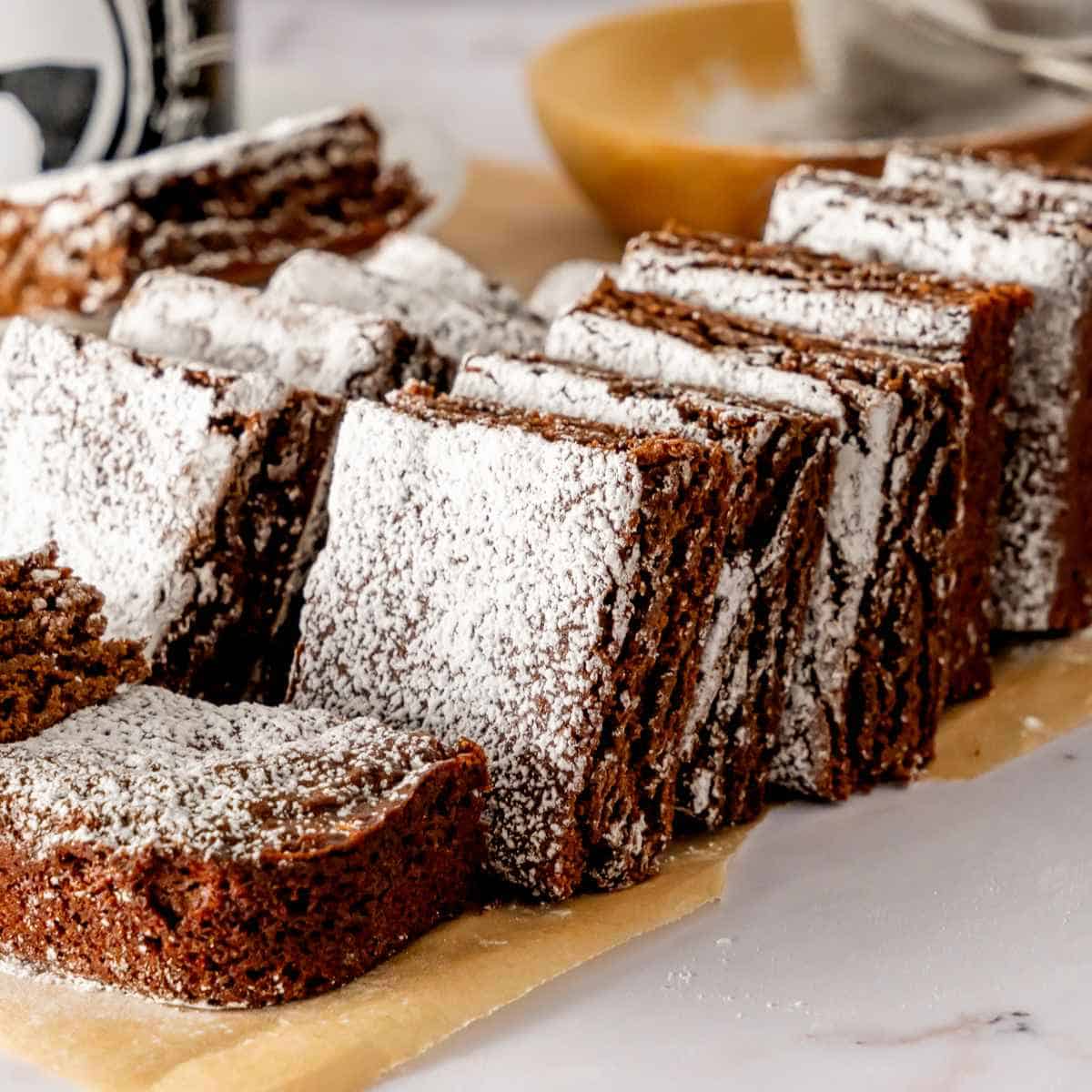 Gingerbread Brownies with powdered sugar sliced and resting on parchment paper.