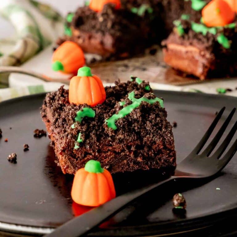 A pumpkin patch brownie square on a black plate topped with Oreo crumbles and candy pumpkins.