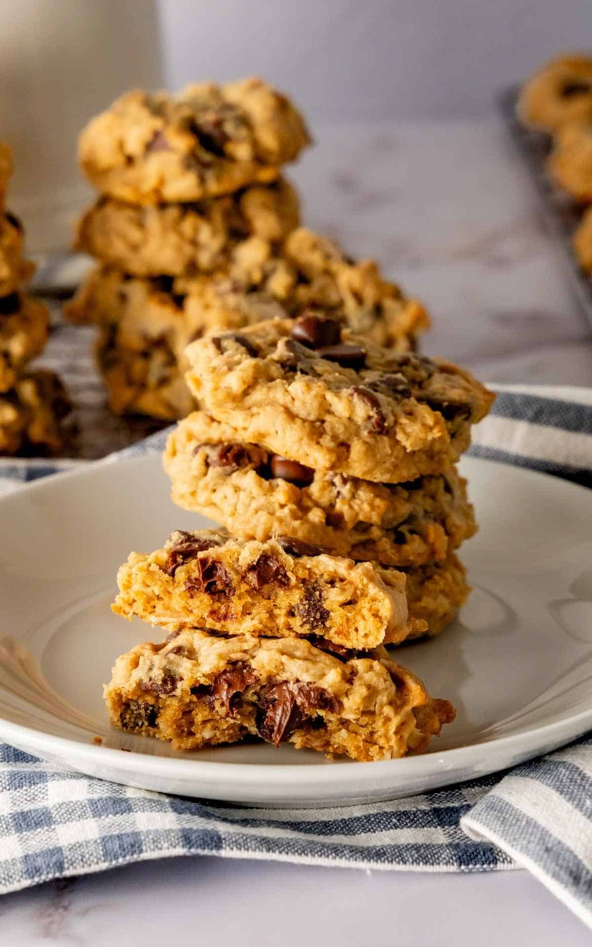 A short stack of peanut butter cookies with chocolate chips with a broken cookie on a plate.