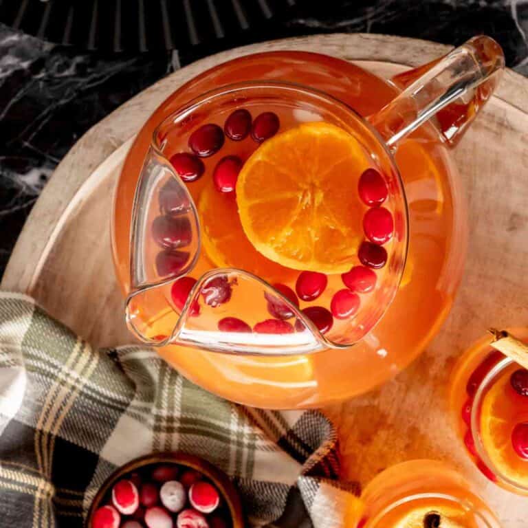 A bowl of cranberries next to a serving pitcher of cranberry tea.
