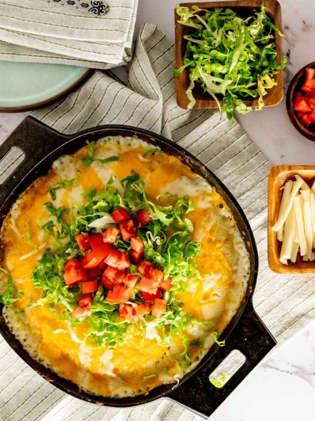 Cast iron skillet with impossible taco pie topped with tomatoes, lettuce, and cheese.