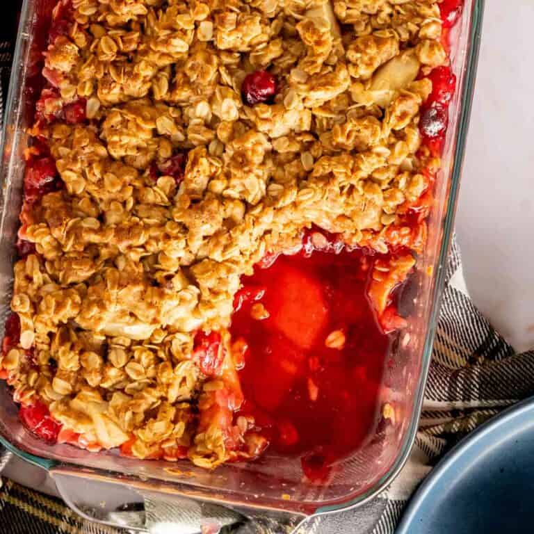 Baked cranberry apple crumble with a serving removed and set on a plate.