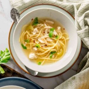 Chicken noodle soup with breadsticks and gray linen napkins.