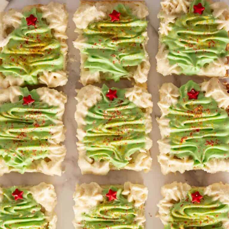 Twelve Christmas cookie bars decorated with green buttercream trees.