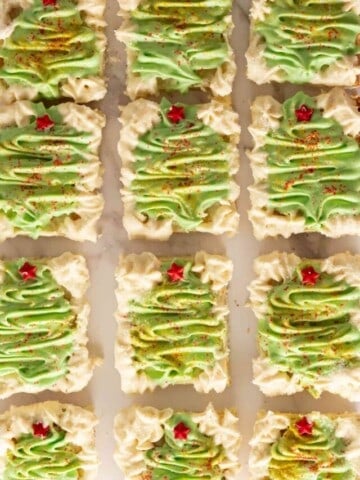 Twelve Christmas cookie bars decorated with green buttercream trees.