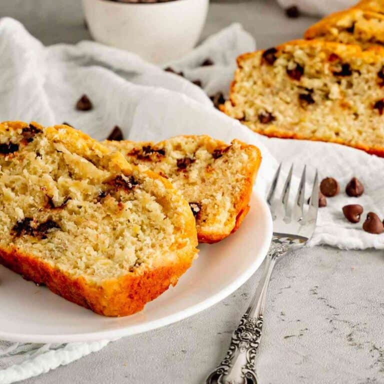 Two slices of chocolate chip banana bread on a white plate with cut slices in the background.