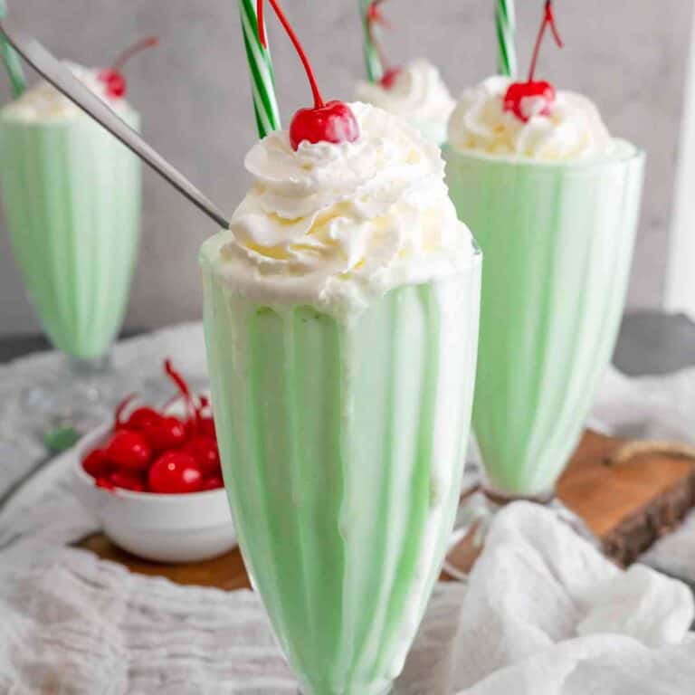 Close up of a old fashioned milkshake glass with a shamrock shake topped with whipped cream and a cherry.