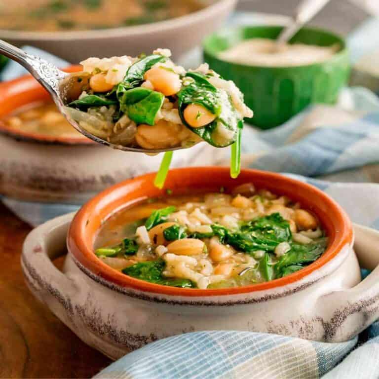 A spoon lifted out of a bowl of white bean and spinach soup.