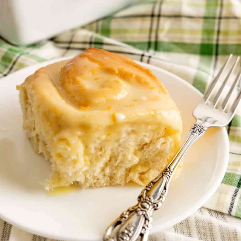 A sweet orange roll on a plate with a decorative fork.
