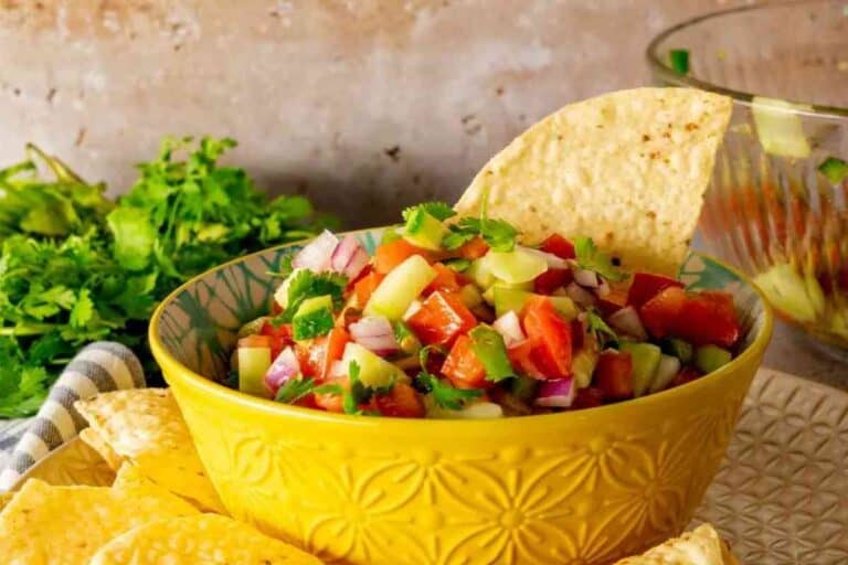 Cucumber salsa in a yellow serving bowl with a tortilla chip stuck in it.