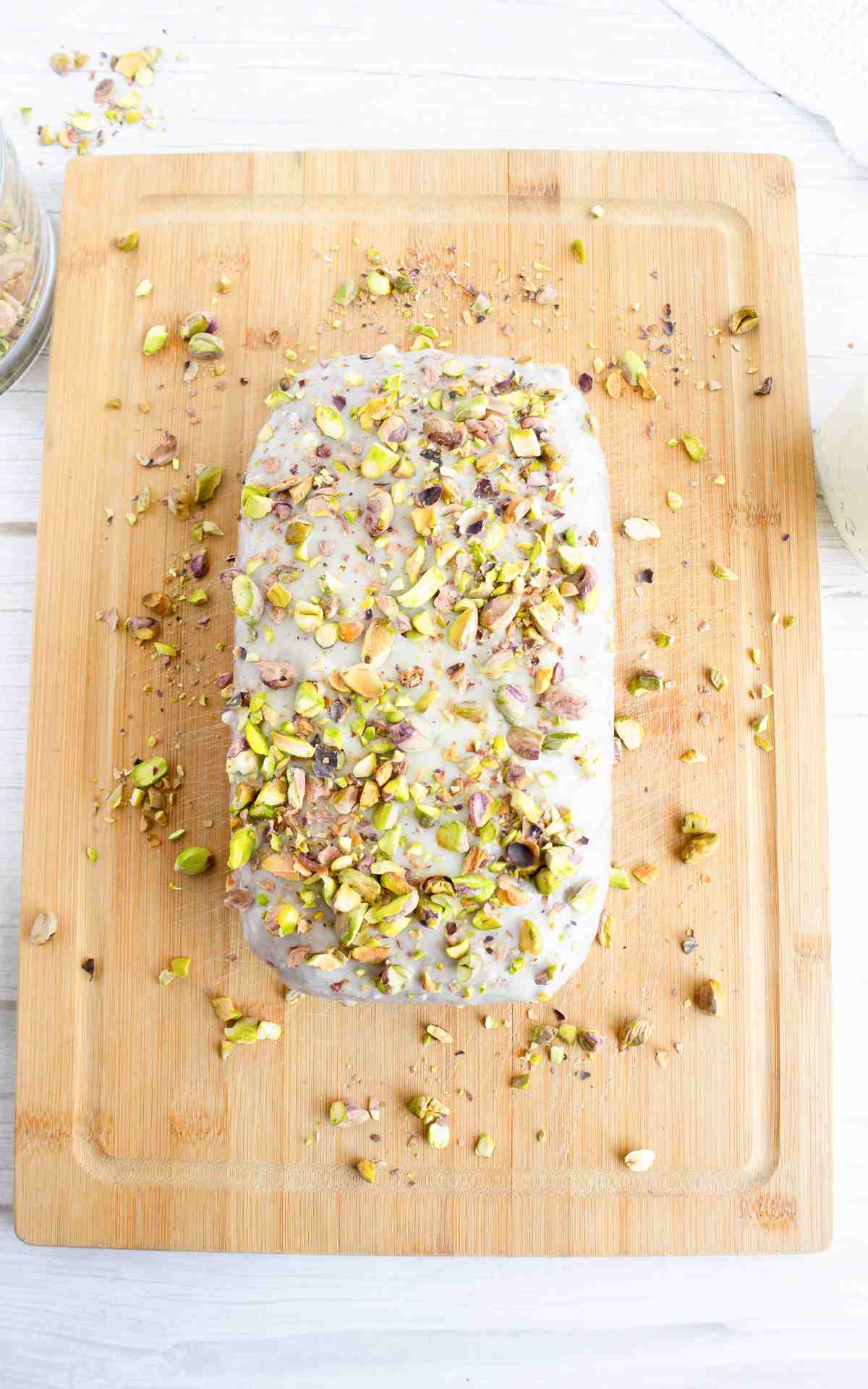 An uncut iced pistachio bread loaf on a wooden serving board.