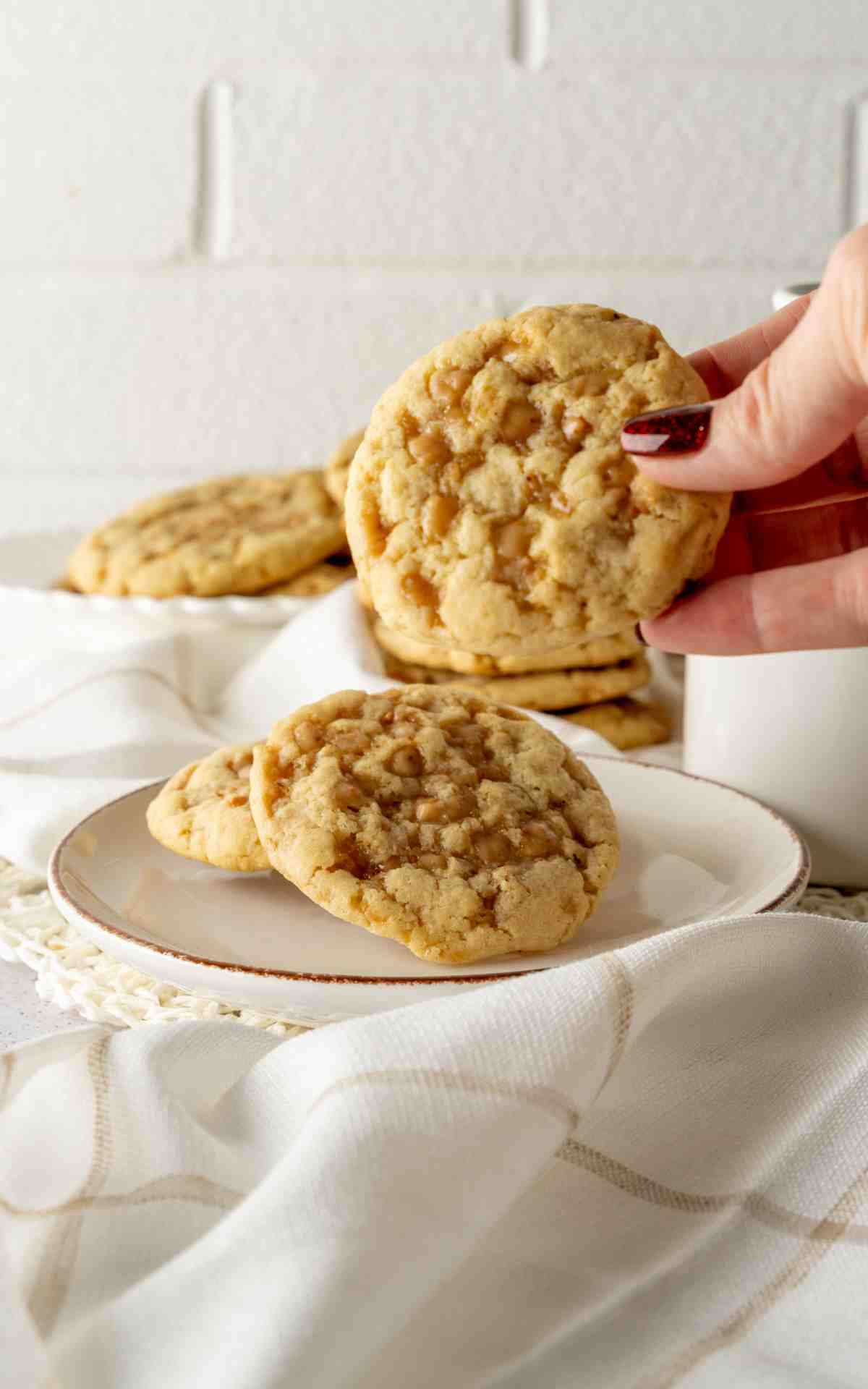 A manicured hand picking up a large toffee cookie.