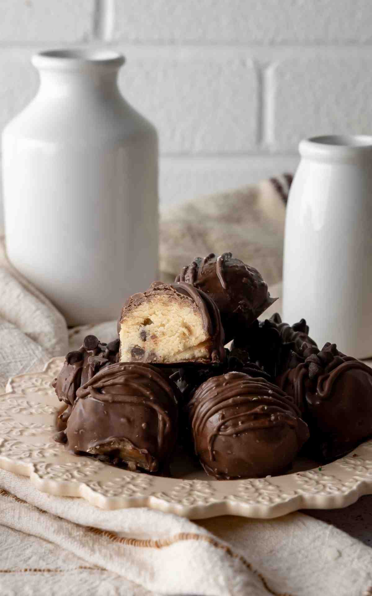 Chocolate dipped edible cookie dough balls on a plate with one cut open.