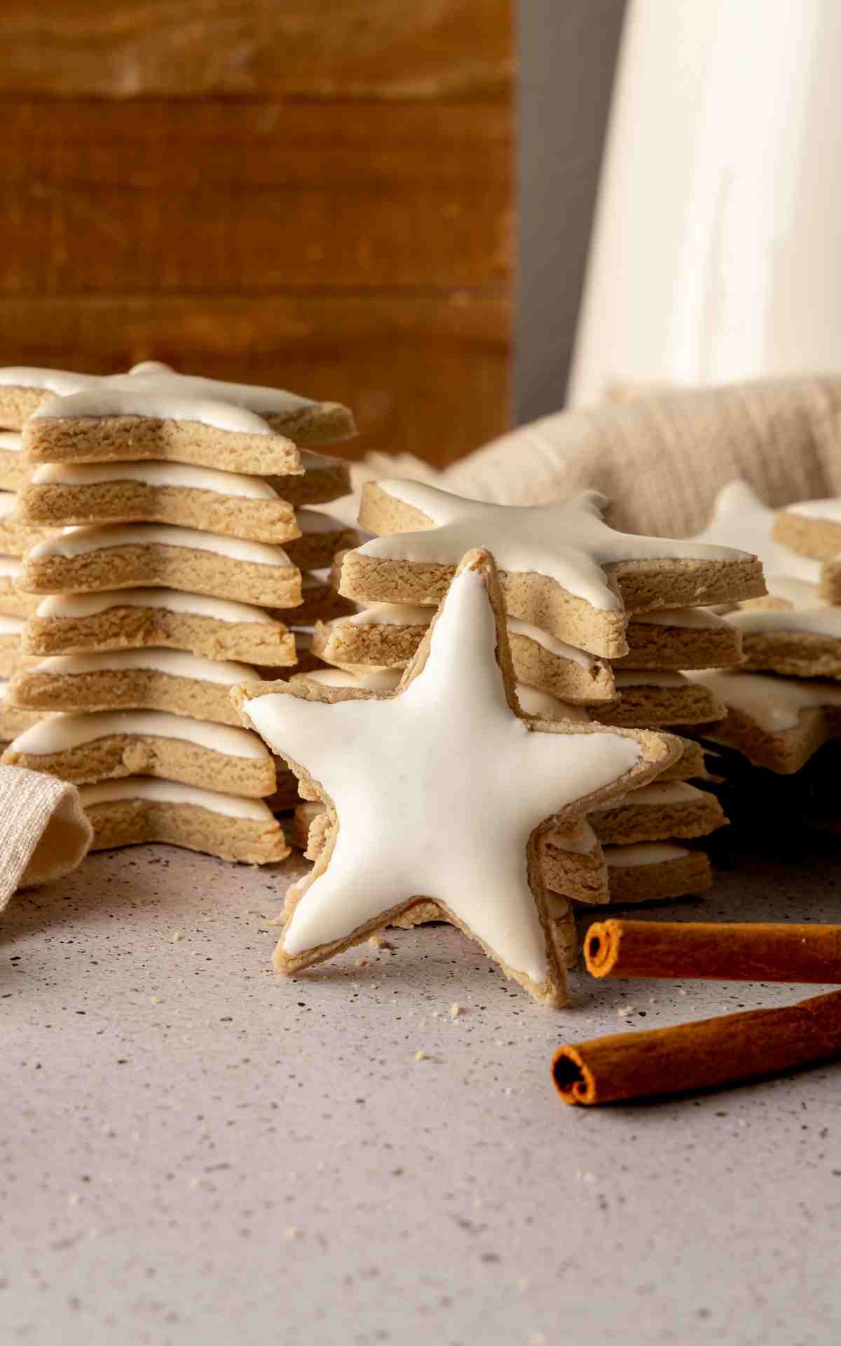 A German cinnamon star cookie propped in front of stack of cookies with meringue topping..