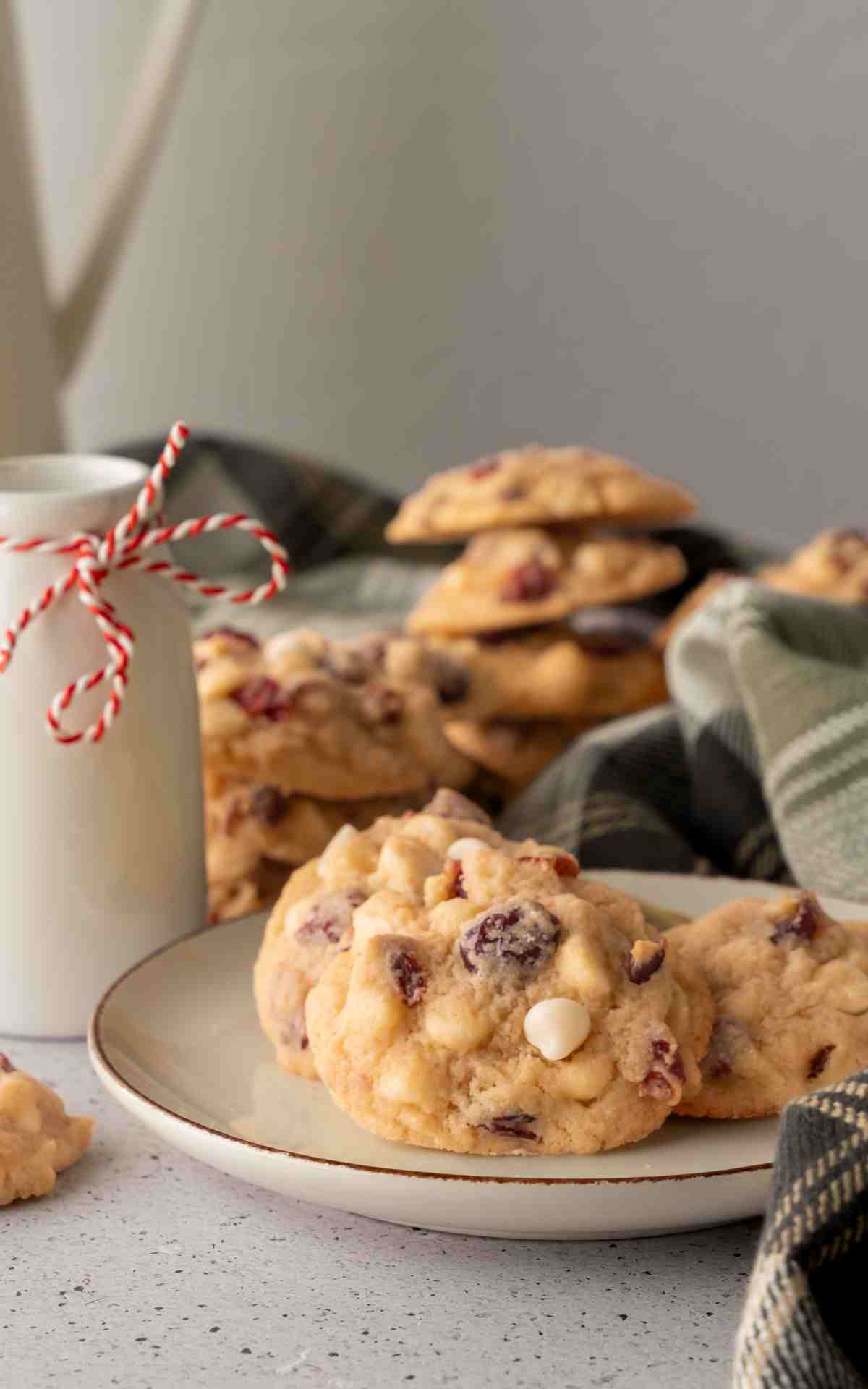 A plate with three white cranberry cookies with a mug of milk.