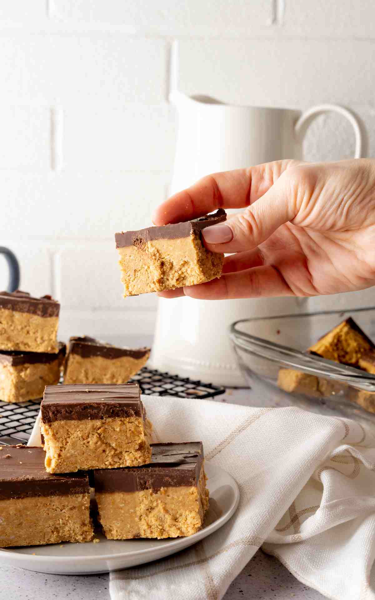 A hand holding a no bake peanut butter bar above a plate.