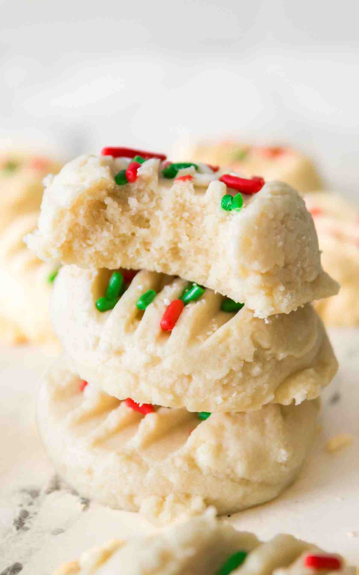 A stack of whipped shortbread cookies with Christmas sprinkles.
