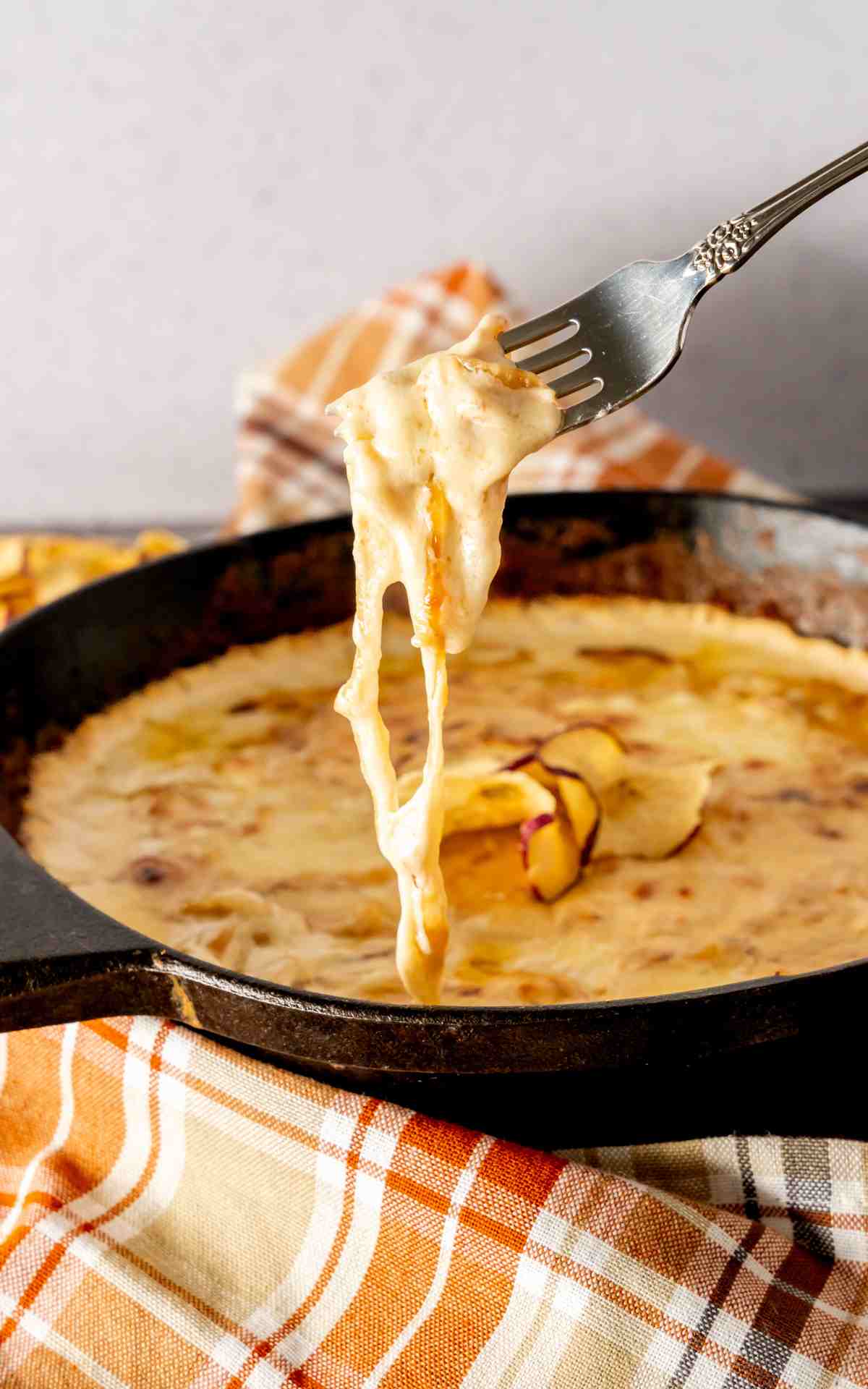A fork with melted cheese in a cast iron skillet.