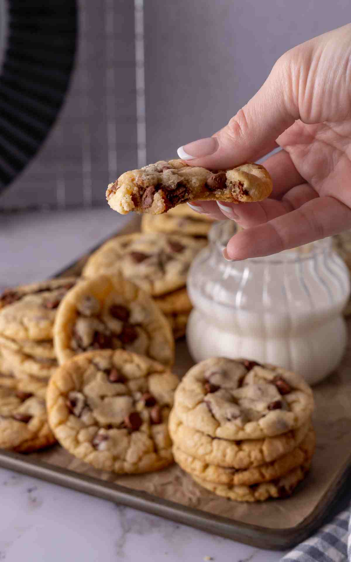 A hand holding up a bitten into chocolate chip cookie to show the inside.