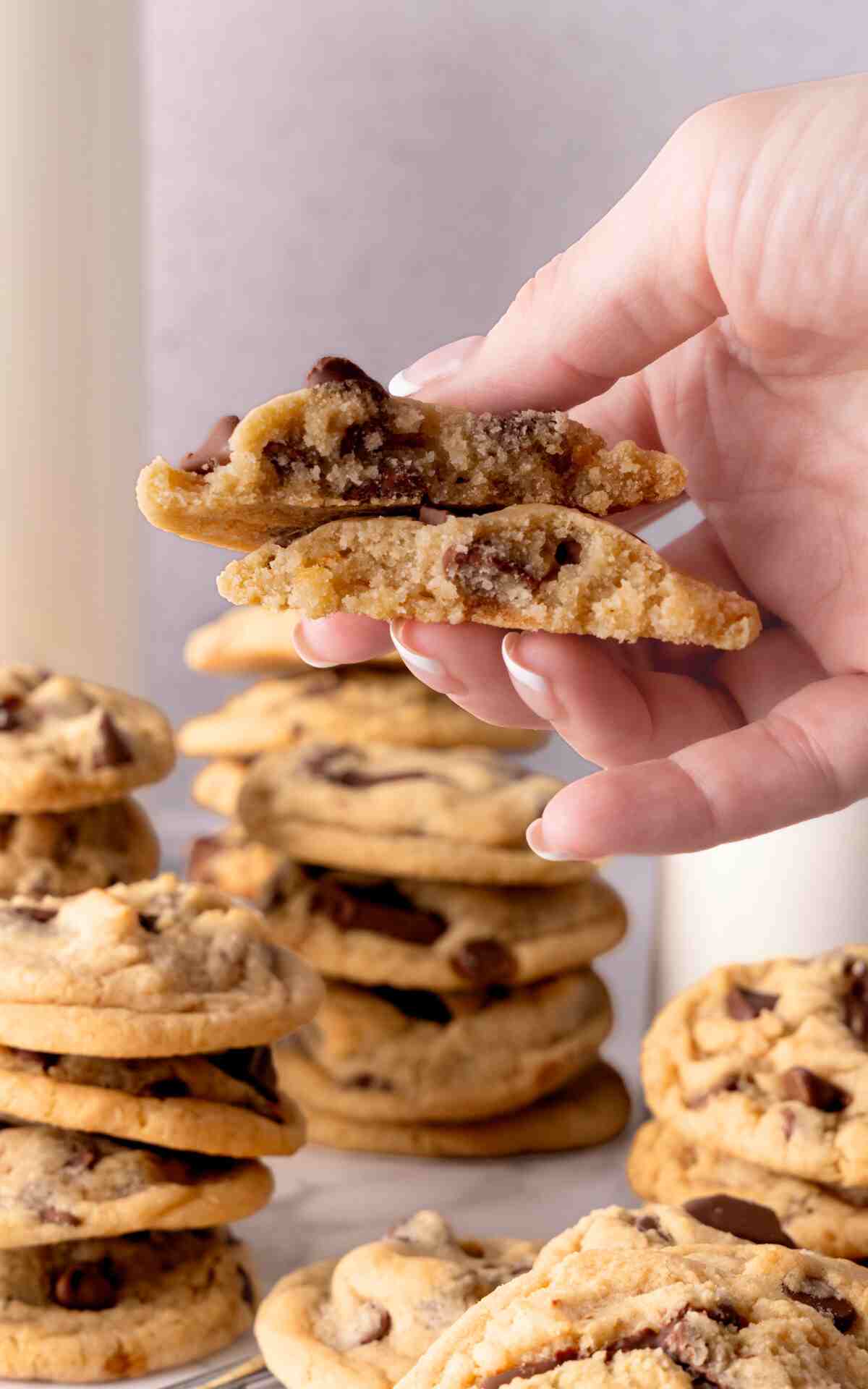 A hand holding up a broken in half eggless chocolate chip cookie.