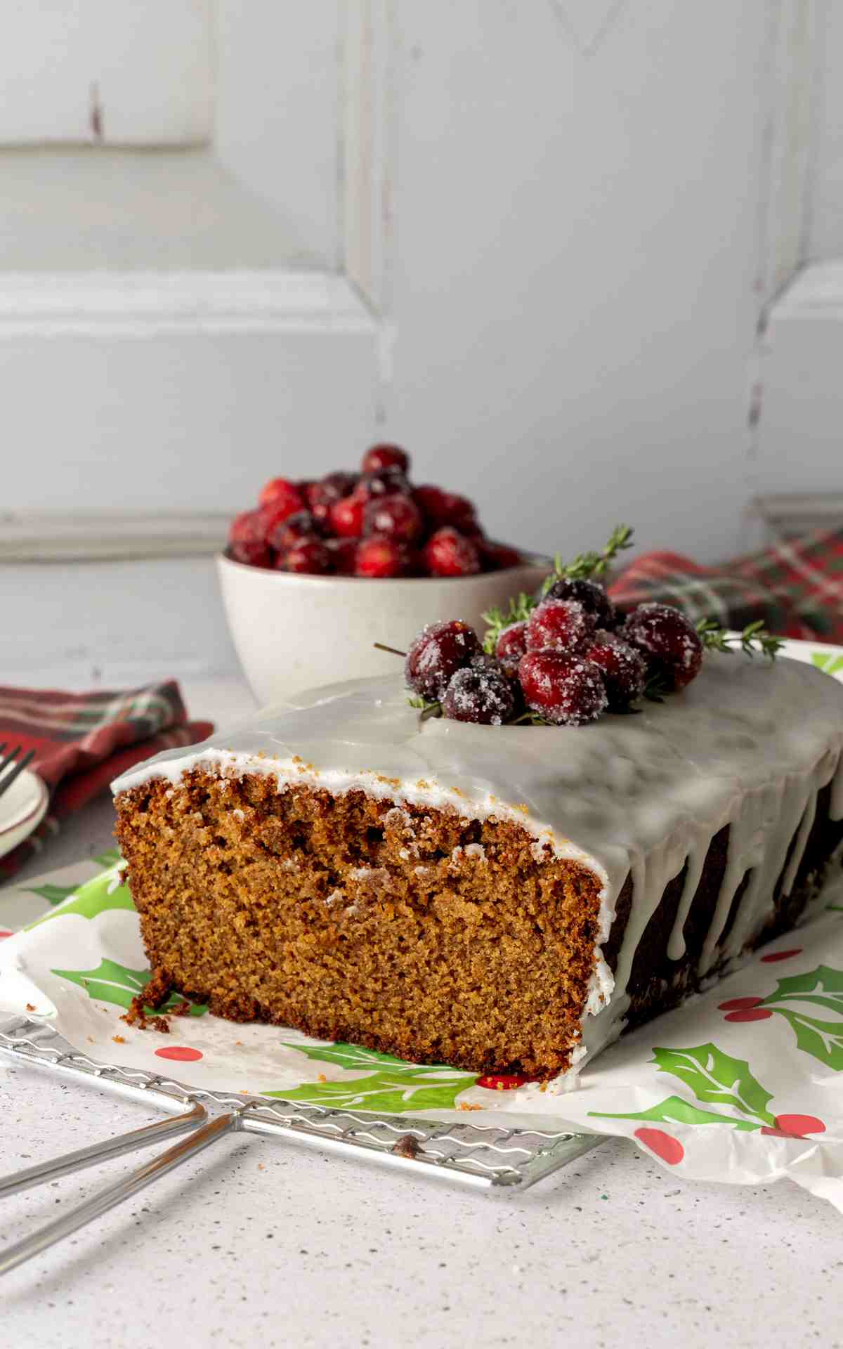 A slice taken off the end of a gingerbread loaf cake topped with glaze and cranberries.