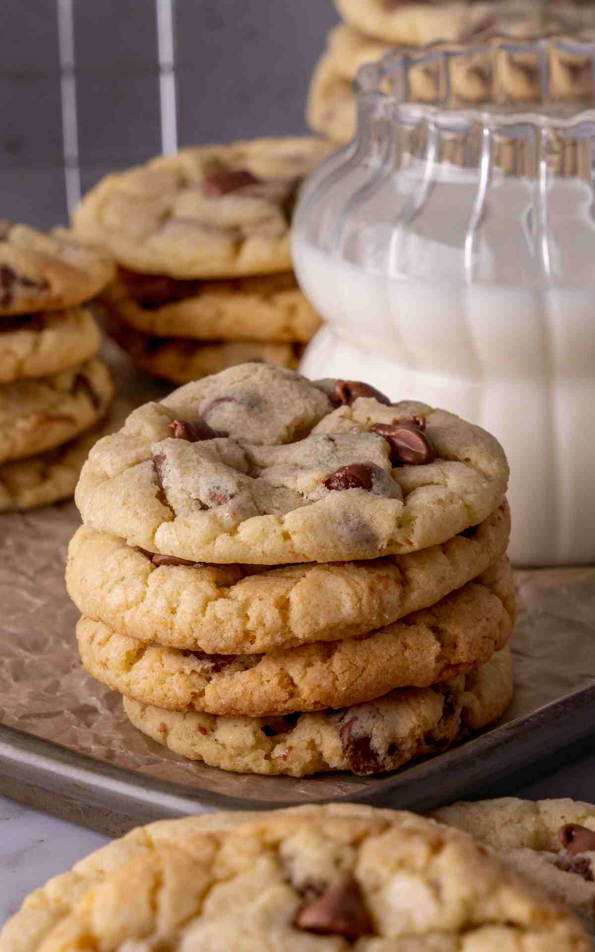 A stack of sour cream chocolate chip cookies on a baking pan with a glass of milk.