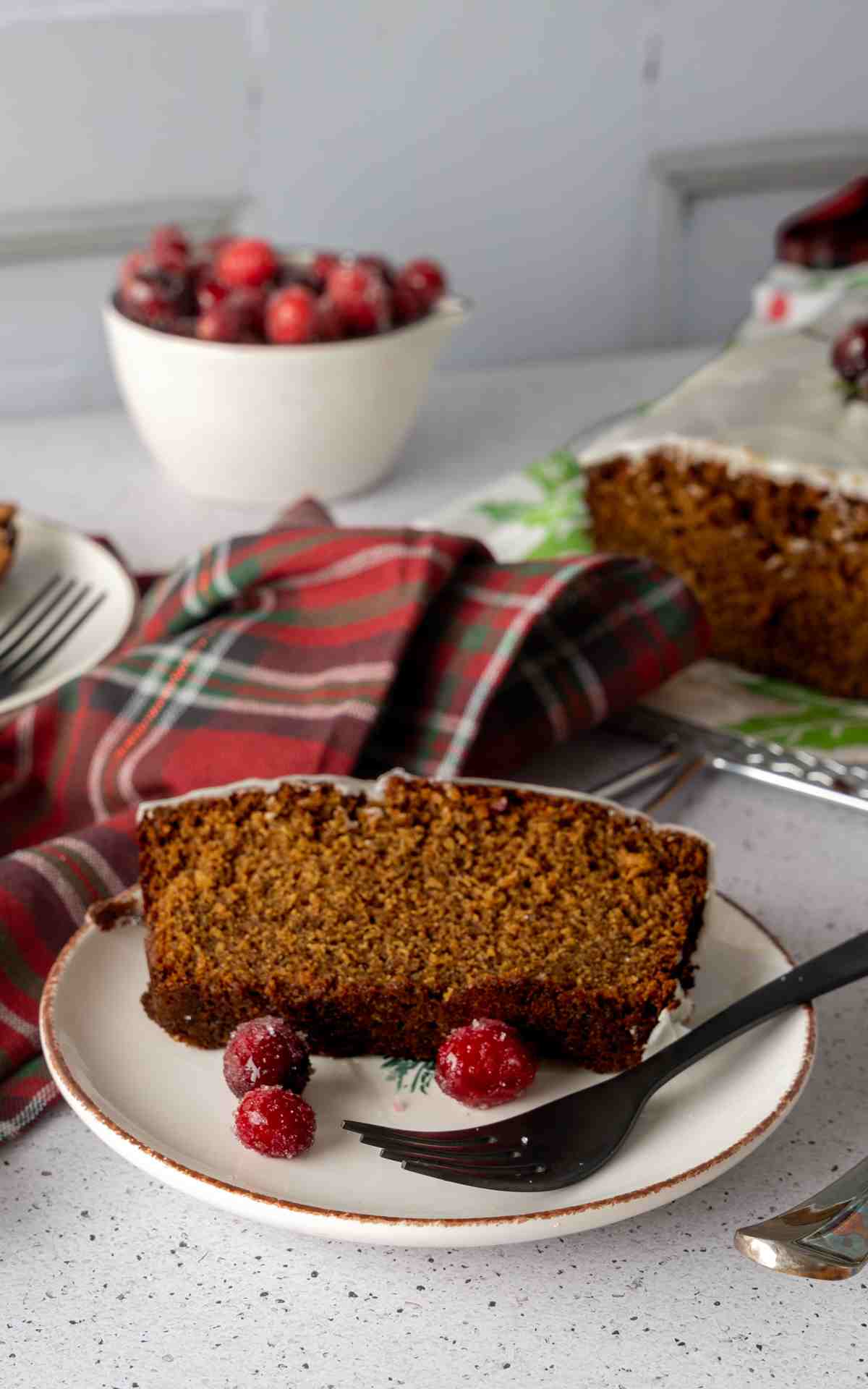 An iced slice of gingerbread loaf on a plate with sugared cranberries.