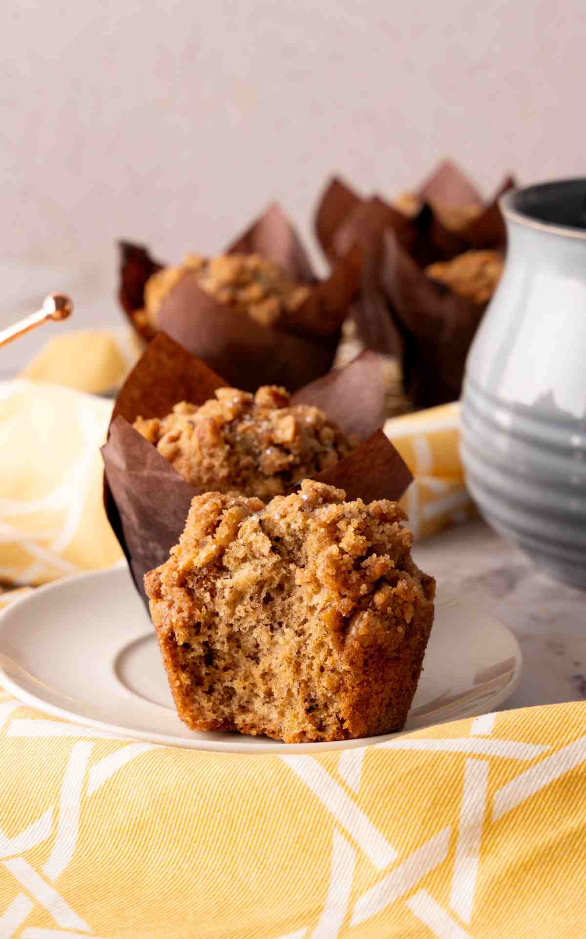 An unwrapped banana muffin with a crunchy walnut topping on a white plate.