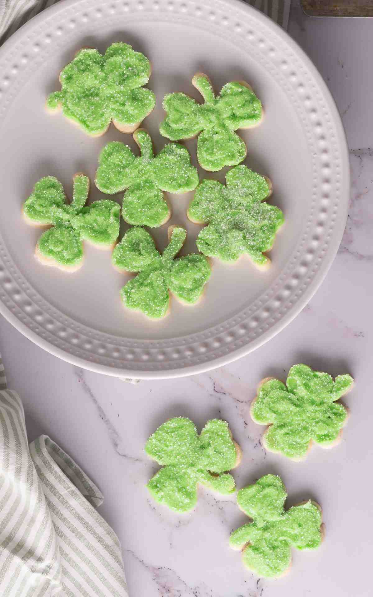 Shamrock cutout sugar cookies on a plate and frosted with buttercream and sprinkles.