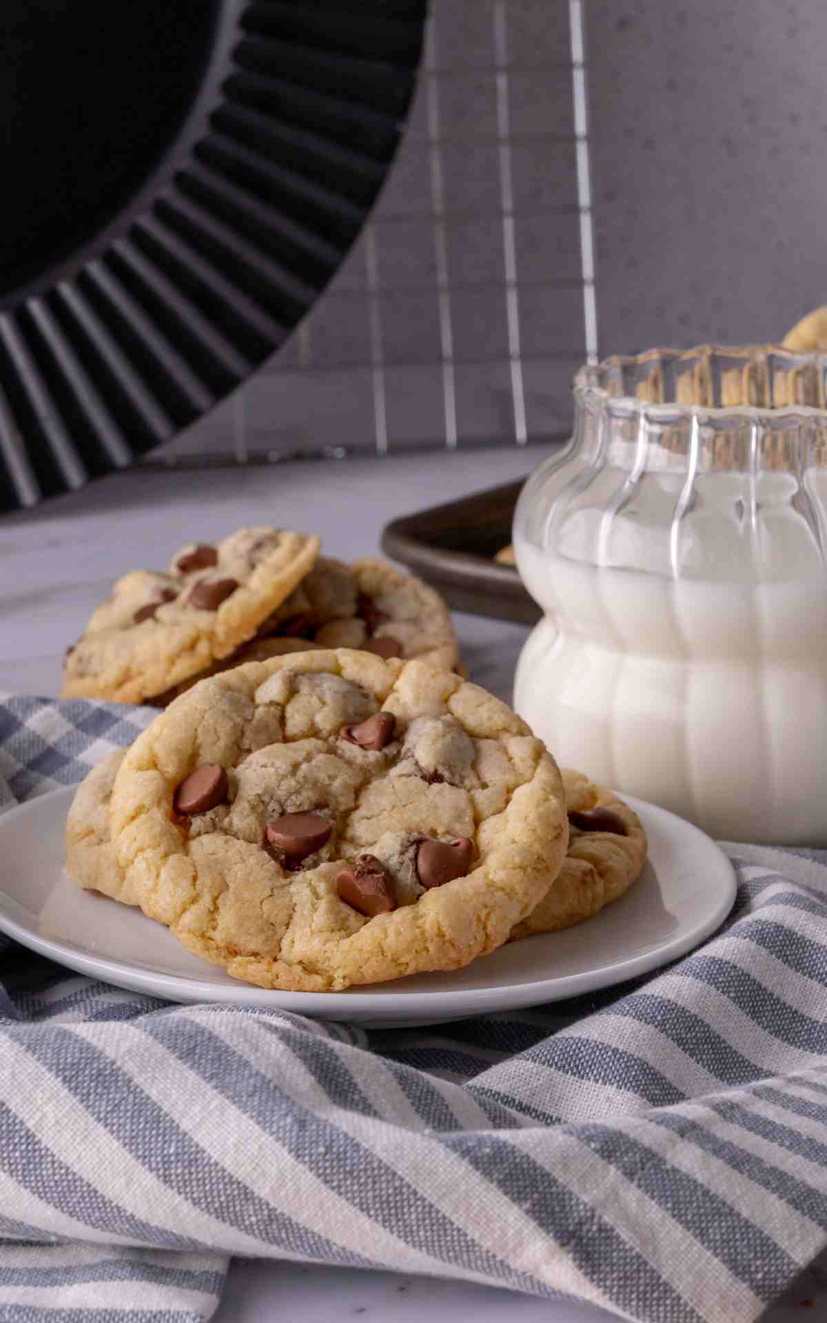 Three sour cream chocolate chip cookies on a white plate with a glass of milk.