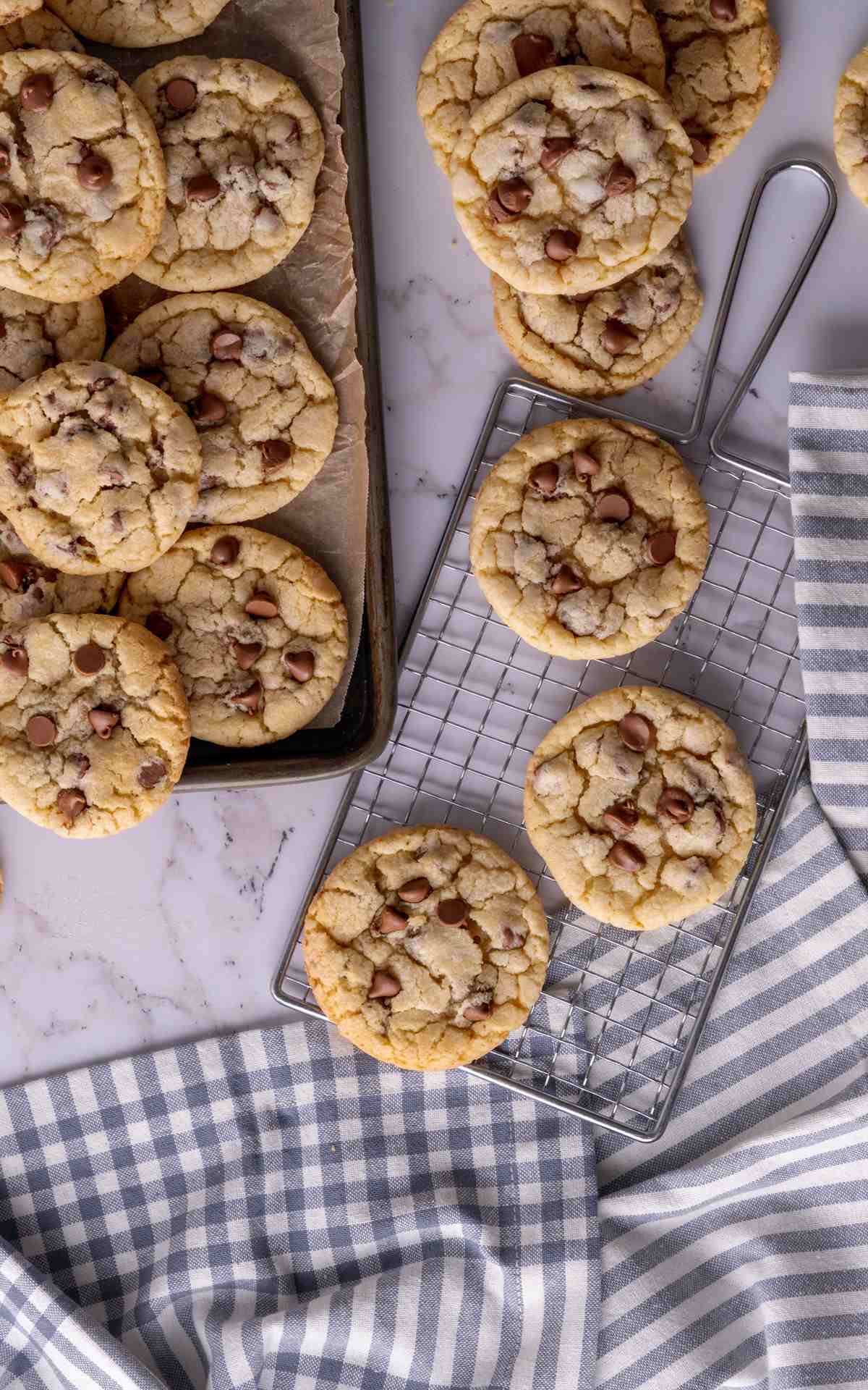 thin chocolate chip cookies on a cooling rack with a sheet pan full of cookies.
