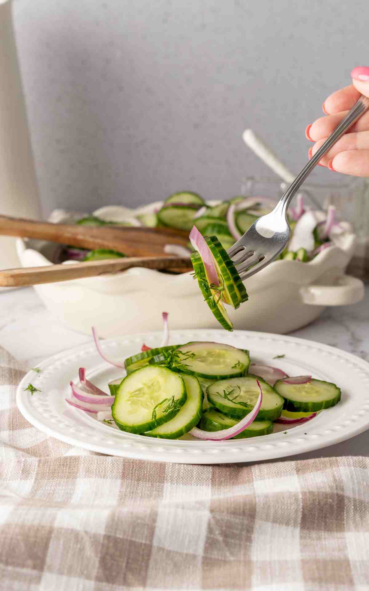 A fork stuck in cucumber salad over a plate.