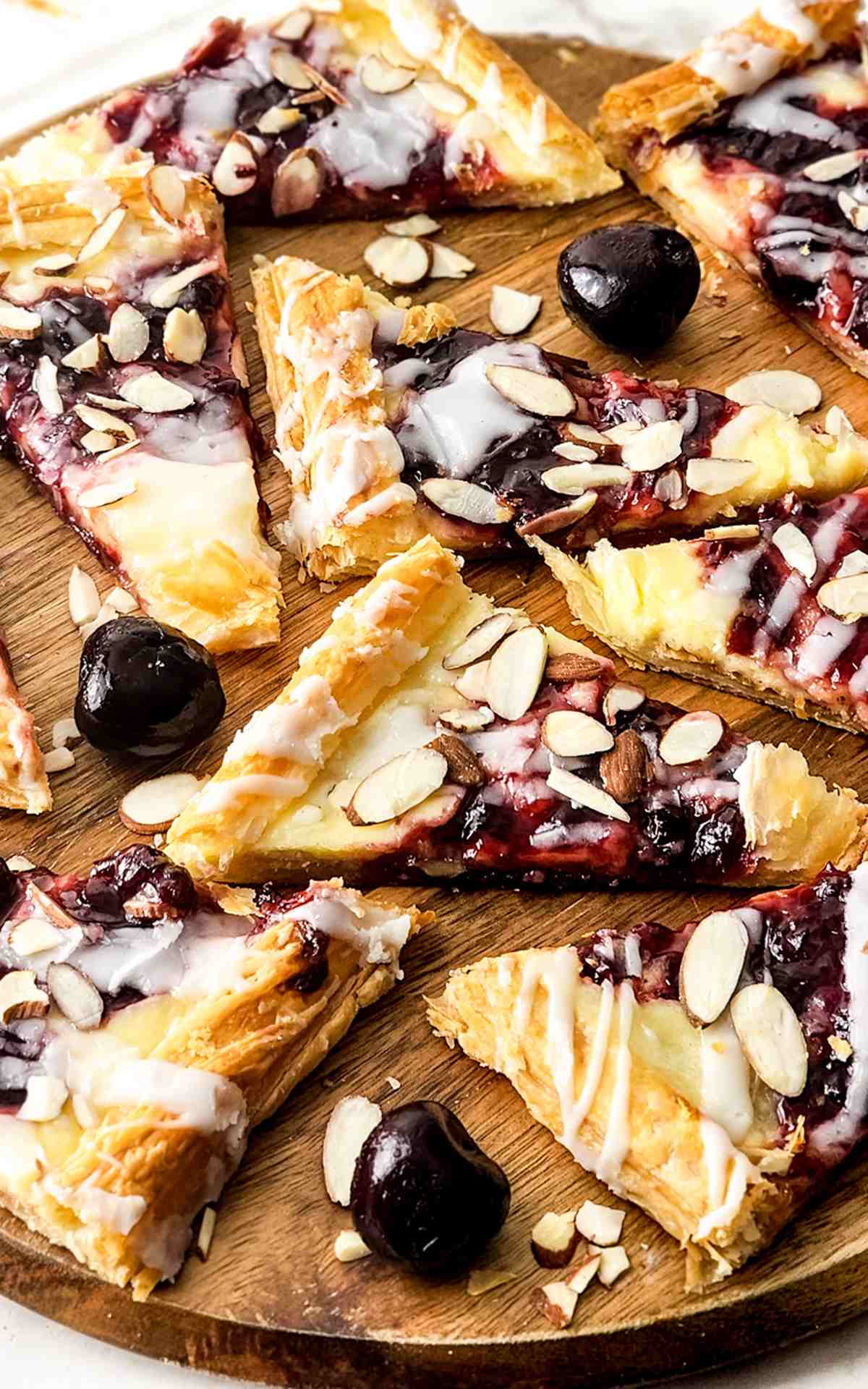 A wooden board with cherry cheese danishes on them.