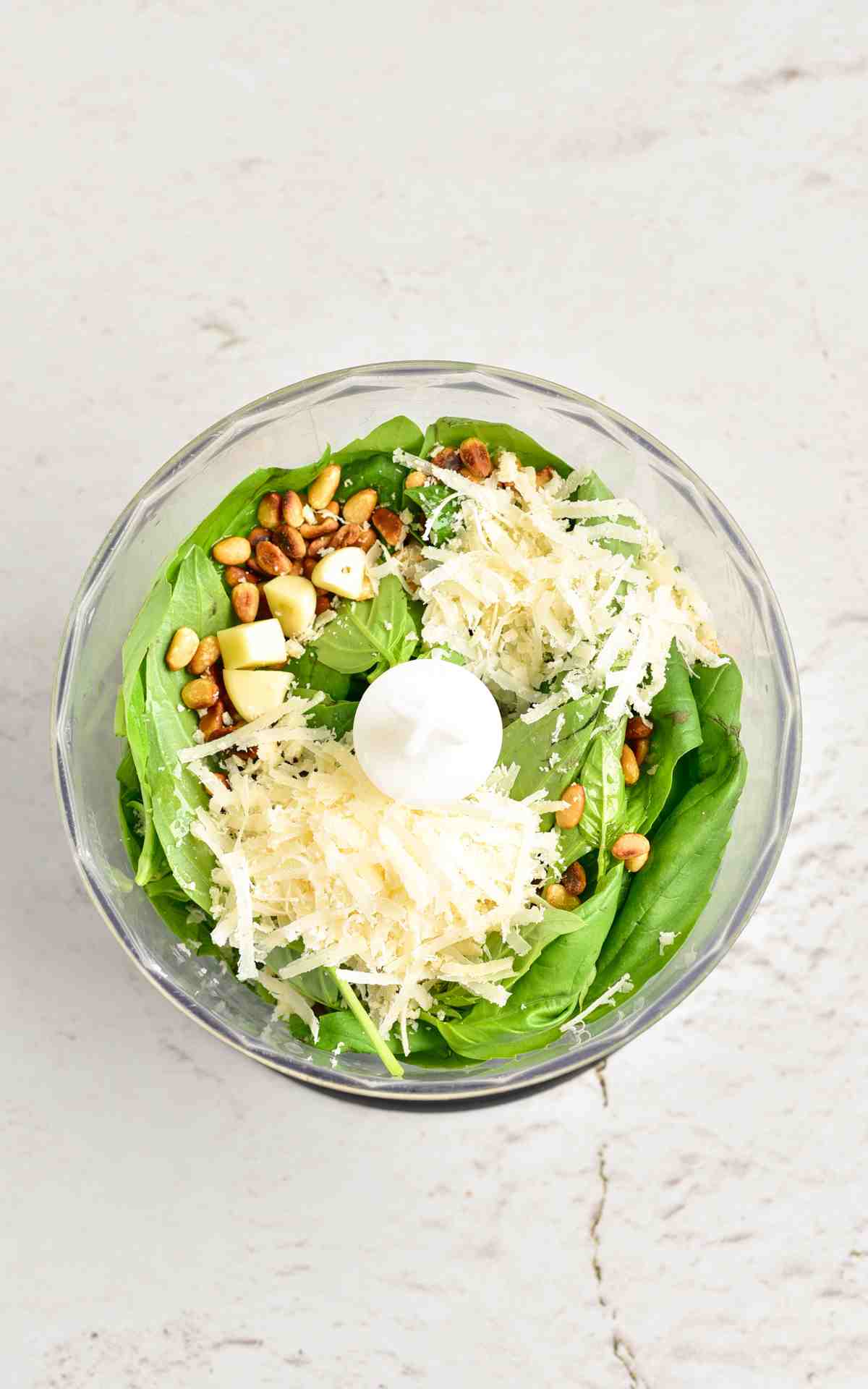 Ingredients for basil pesto in a food processor before being blended.