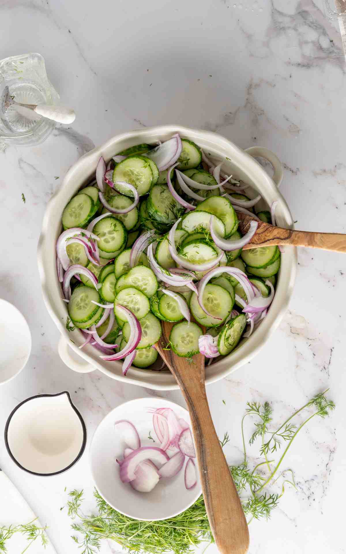 Serving utensils in a bowl of sliced cucumbers and onions with apple cider vinegar.