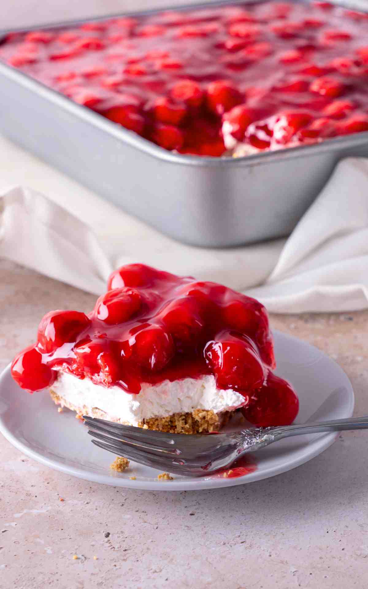 A fork cut into a square of no bake cherry delight on a plate.
