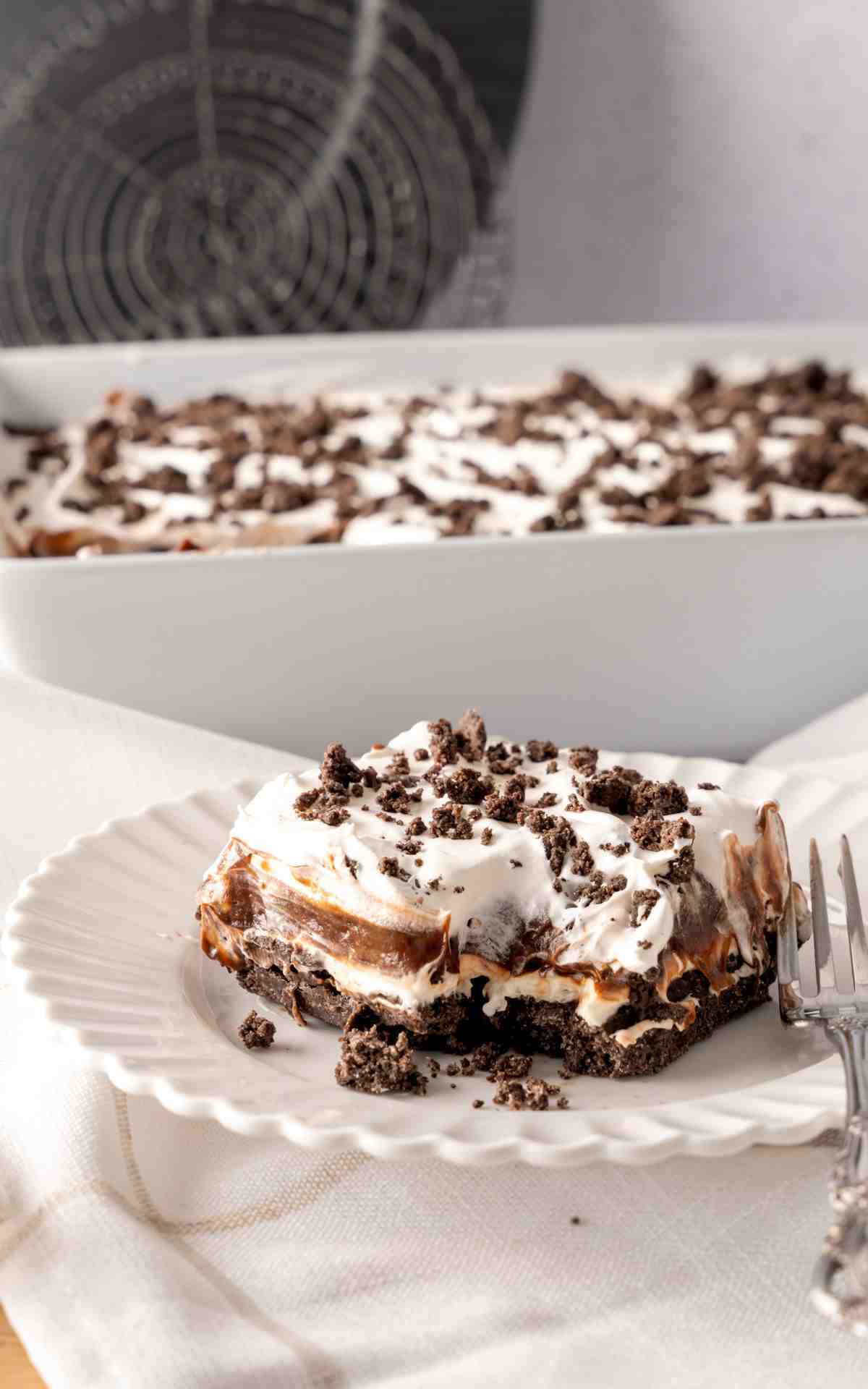 A saucer with a slice of no bake chocolate lasagna with. a fork cut into the slice.
