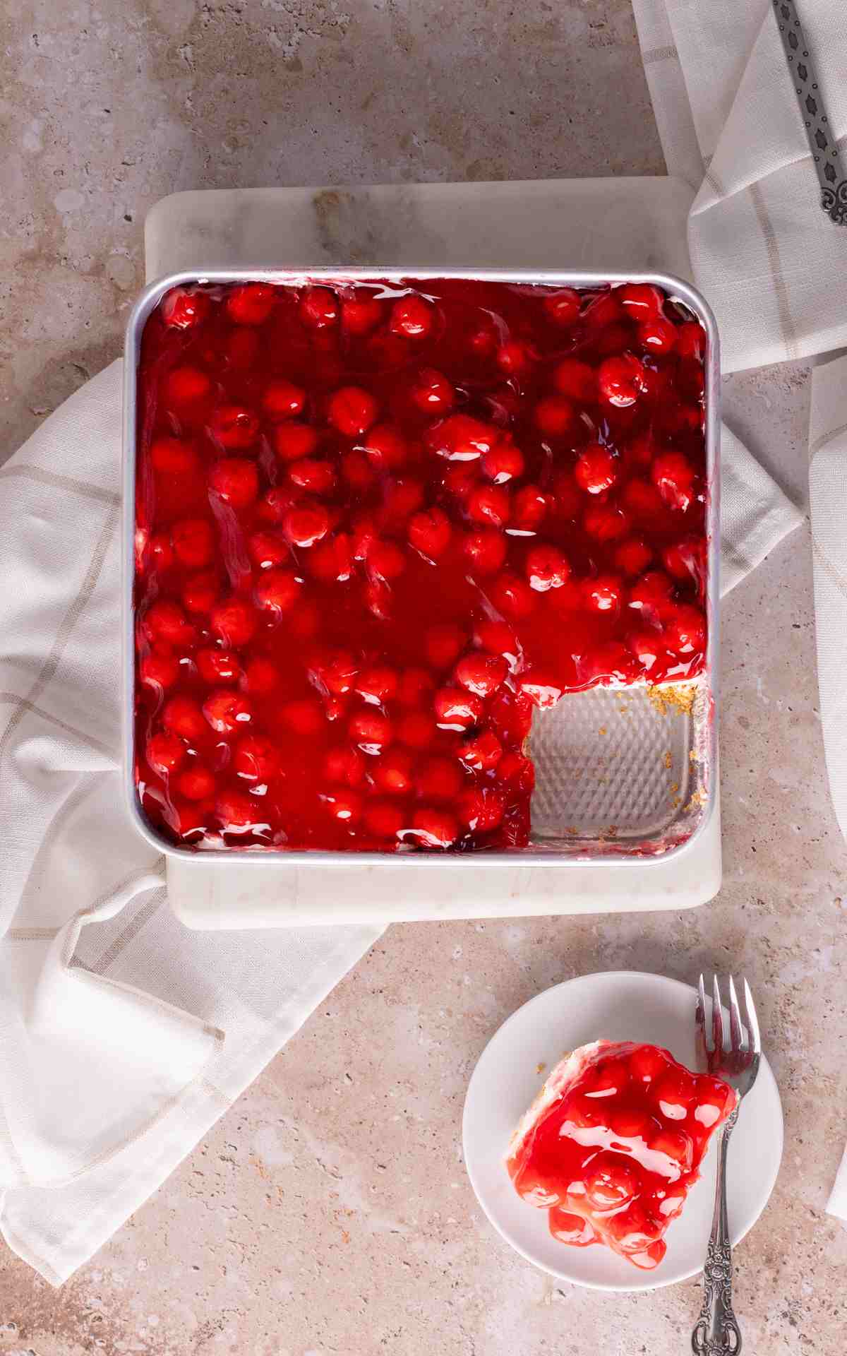 A slice of cherry yum yum on a plate with the baking dish next to it.