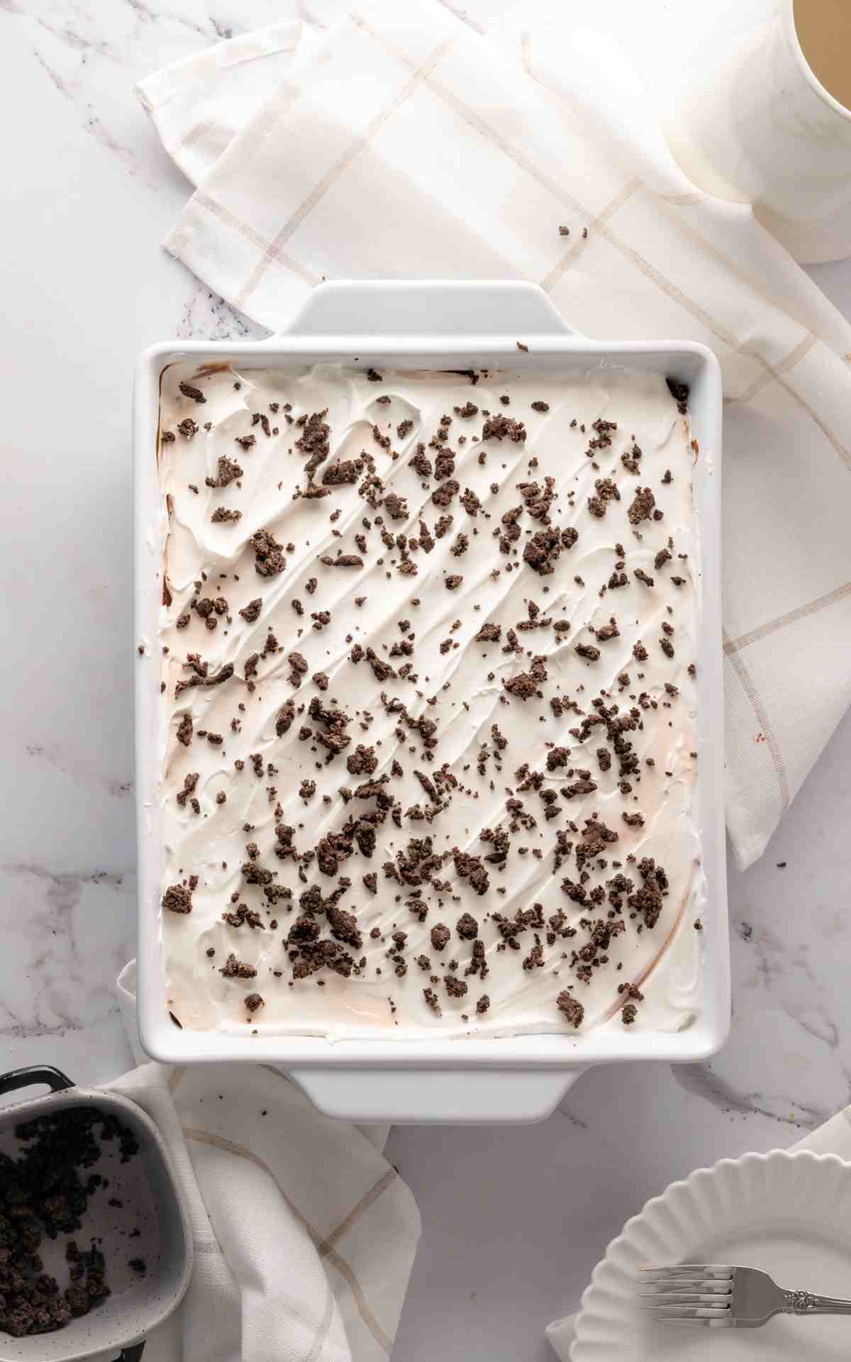 Oreo cookie crumbs sprinkled on top of Cool Whip in a 9 by 13 dish.