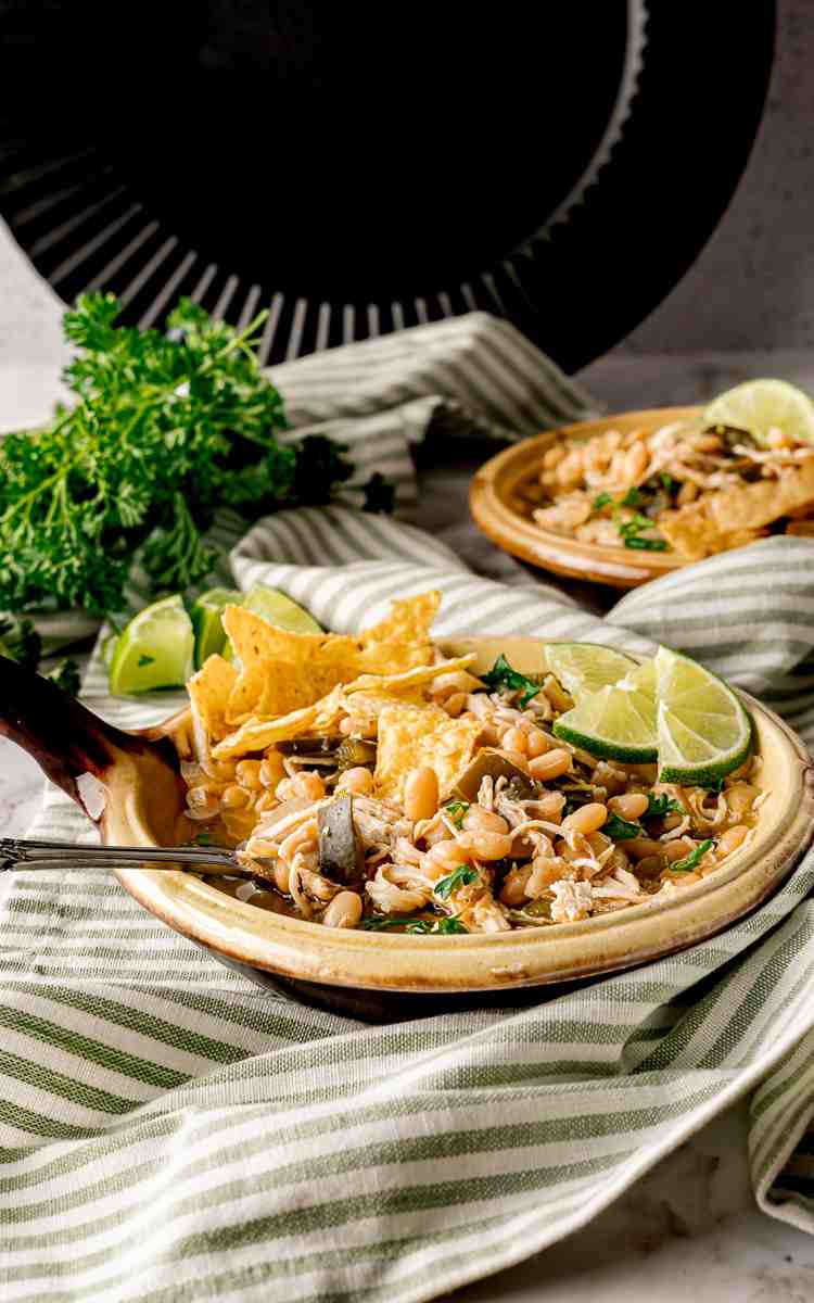 A bowl of green chicken chili with tortilla chips and lime slices.